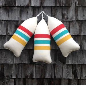 May include: Three white striped pillows with red, yellow, and turquoise stripes hanging on a dark wood wall.
