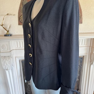 May include: A black blazer with a high collar and gold buttons. The tailored jacket features a V-neckline and decorative stitching on the front. The sleeves have a cuff detail. This classic blazer is suitable for formal or business attire.