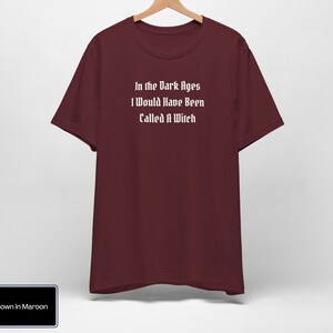 May include: A maroon t-shirt with the text "In the Dark Ages I Would Have Been Called A Witch" printed in white.