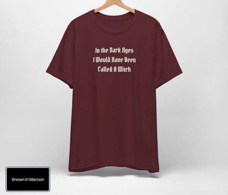 May include: A maroon t-shirt with the text "In the Dark Ages I Would Have Been Called A Witch" printed in white.