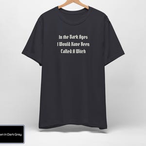 May include: Dark grey t-shirt with the text "In the Dark Ages I Would Have Been Called A Witch" printed in white.