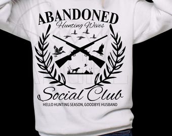 Op de afbeelding: Witte sweatshirt met een zwart grafisch ontwerp. Het ontwerp bevat gekruiste geweren, vogels en de tekst "ABANDONED Hunting Wives Social Club". De zin "HELLO HUNTING SEASON, GOODBYE HUSBAND" is ook opgenomen.