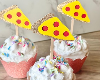 May include: Three cupcakes in pink scalloped wrappers topped with white frosting, colorful sprinkles, and pizza slice toppers. Each topper features a yellow pizza slice with red pepperoni circles and a gold glitter crust on a wooden stick.