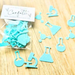 May include: A clear plastic bag containing light blue glittery paper cutouts shaped like science laboratory equipment including microscopes, beakers, and molecular structures, with a white label printed with the text Confetti.
