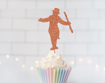 May include: A copper-colored glitter cupcake topper shaped like a silhouette of a person wearing a top hat and holding a cane, inserted into a white frosted cupcake with a pastel-striped paper liner. The topper features a textured finish.