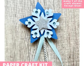 May include: A paper craft kit featuring a blue star base topped with a white snowflake, a silver glitter star, and light blue sequins. A chevron-patterned stick extends from the bottom, adorned with two light blue ribbons. Text reads: PAPER CRAFT KIT PRE-CUT CRAFTS FOR KIDS. Includes everything needed to make 1 of the craft shown! Except Glue!