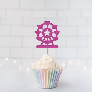 May include: A pink glittery ferris wheel cupcake topper featuring a central star cutout, attached to a thin wooden pick, inserted into a white frosted cupcake with a pastel-coloured pleated paper liner, set against a white tiled background.
