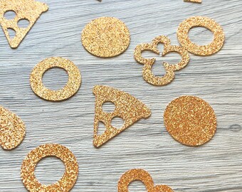 May include: A collection of copper-colored glitter confetti pieces in various shapes, including mushrooms, pizza slices, solid circles, open rings, and four-leaf clover outlines, scattered across a light-colored wood grain surface.