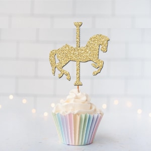 May include: A gold glitter carousel horse cupcake topper featuring a silhouette of a horse attached to a central pole, inserted into a cupcake with white frosting and a pastel-colored pleated paper liner, creating a decorative party accent.