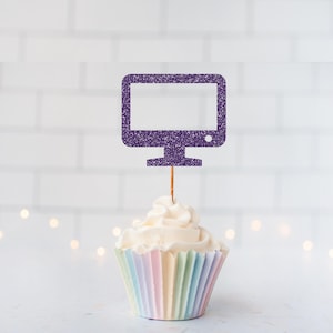 May include: A purple glitter computer monitor cupcake topper on a thin wooden pick, inserted into a white frosted cupcake with a pastel striped paper liner. The monitor shape features a small circular detail in the bottom right corner.