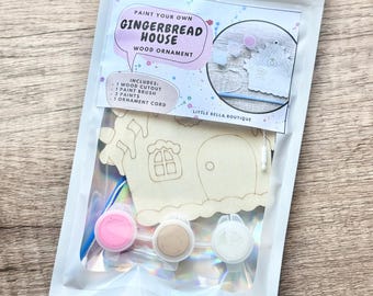 May include: A paint your own gingerbread house wood ornament craft kit in a sealed pouch. The kit includes one wooden house cutout, one paint brush, three small paint pots in pink, tan, and white, and one ornament cord for hanging the finished piece.