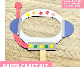 May include: A paper craft kit featuring a white astronaut helmet cutout with a pink antenna, blue side panels, and a gray control panel with yellow and green circles. The helmet is decorated with small yellow, orange, red, pink, and peach stars.
