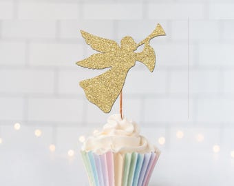 May include: A gold glitter angel cupcake topper featuring a figure with wings playing a trumpet, attached to a thin wooden pick, inserted into a white frosted cupcake with a pastel-colored pleated paper liner.