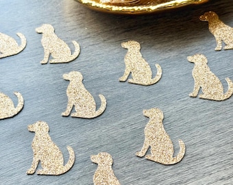 May include: A collection of small, die-cut dog silhouettes made from gold glitter cardstock. The individual dog shapes are scattered across the surface, while a larger pile of the same gold glitter dog cutouts is contained within a gold-toned dish.