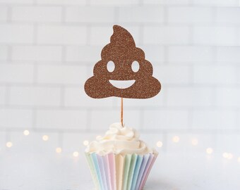 May include: A brown glittery poop emoji cupcake topper attached to a thin wooden stick, inserted into a cupcake with white frosting in a pastel-colored pleated paper liner. The topper features a smiling face with two white eyes and a mouth.