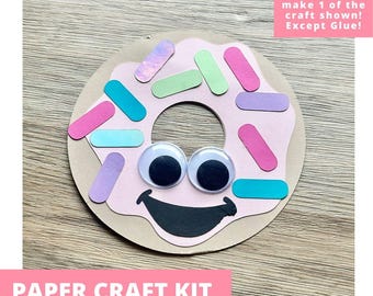 May include: A paper craft kit featuring a circular donut shape with light pink icing, a black smiling mouth, two large googly eyes, and colorful rectangular paper sprinkles in shades of blue, green, purple, and pink. Includes everything needed to make 1 of the craft shown! Except Glue!