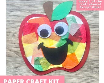 May include: A paper craft kit featuring an apple shape with a red outline, filled with multicolored tissue paper squares. It includes two large white googly eyes, a black paper smile, and a brown stem with a green leaf attached at the top.