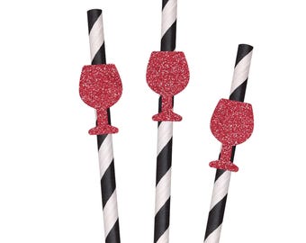 May include: Three drinking straws featuring a black and white diagonal striped pattern. Each straw is adorned with a red glittery cutout in the shape of a wine glass, positioned towards the upper section of the straw, creating a decorative accent.