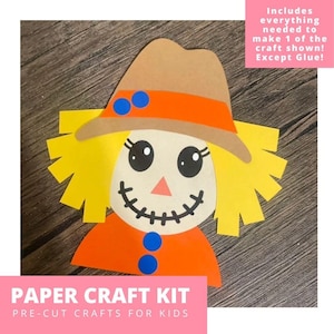 May include: A paper craft kit featuring a scarecrow face with a tan hat, orange band, and blue circles. The scarecrow has yellow paper hair, a cream face, black eyes, a pink triangle nose, and a stitched black mouth. Text reads: PAPER CRAFT KIT PRE-CUT CRAFTS FOR KIDS. Includes everything needed to make 1 of the craft shown! Except Glue!