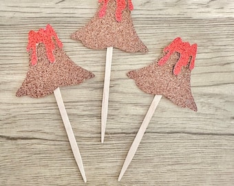May include: Three volcano-shaped cupcake toppers featuring a brown glittery base and a bright red glittery lava flow dripping from the peak. Each cutout is securely attached to a thin, pointed wooden pick for insertion into food items.