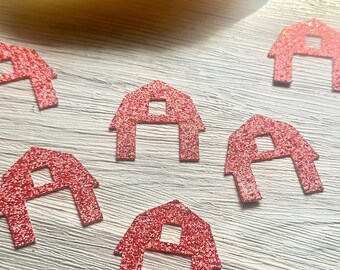 May include: Multiple red glitter barn-shaped cutouts scattered across a surface. Each cutout features a distinct peaked roof silhouette with a small square window opening in the center, crafted from a textured, sparkling red material.