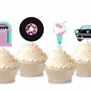 May include: Four cupcakes with retro-themed toppers. The toppers include a jukebox, a vinyl record with musical notes, a milkshake, and a classic car. The cupcakes have white frosting and are in paper liners. The toppers are in shades of pink, teal, and black.