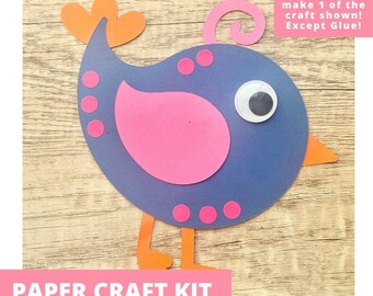 May include: A paper craft kit featuring a blue bird shape with a pink wing, orange tail and feet, a pink crest, and a googly eye. The bird is decorated with small pink circles. Text on the image reads: Includes everything needed to make 1 of the craft shown! Except Glue! PAPER CRAFT KIT PRE-CUT CRAFTS FOR KIDS
