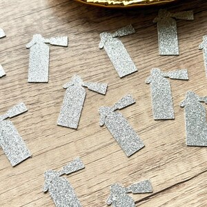 May include: A collection of silver glitter fire extinguisher shaped cutouts scattered across a surface. The cutouts feature a textured, sparkling finish and are arranged in a loose pattern, with a pile of additional cutouts resting in a gold bowl.