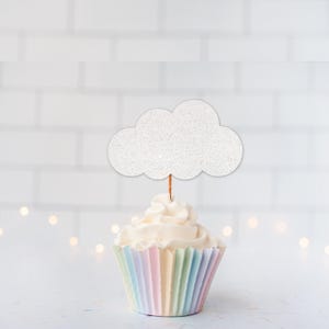 May include: A cupcake topper featuring a white glittery cloud shape attached to a thin wooden pick. The cupcake is encased in a pleated paper liner with vertical stripes in pastel shades of pink, yellow, blue, and green, topped with white frosting.