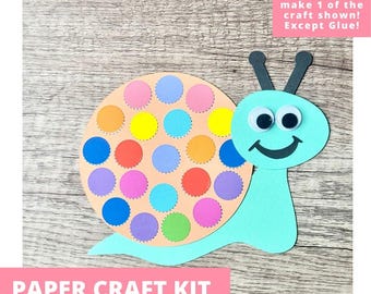 May include: A paper craft kit featuring a snail made of light blue cardstock with a large peach-colored circular shell. The shell is decorated with numerous small, colorful paper circles in shades of yellow, orange, red, blue, purple, and green. The snail has two black antennae and two googly eyes with a black smiling mouth.
