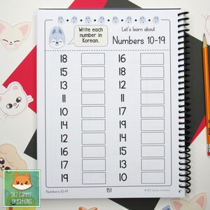 Pu&ograve; includere: Una pagina di quaderno a spirale con il titolo "Impariamo i numeri 10-19". La pagina presenta caselle numerate per scrivere in coreano. Il quaderno ha una rilegatura a spirale nera ed &egrave; circondato da adesivi e una matita.