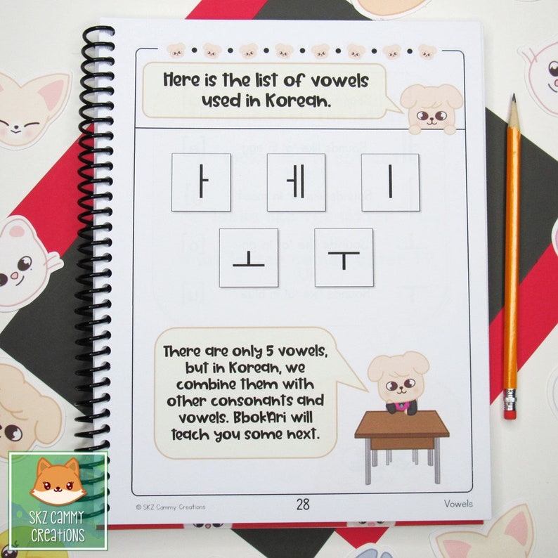 Pu&ograve; includere: Una pagina di quaderno a spirale con esempi di vocali coreane. Il testo recita "Ecco l'elenco delle vocali usate in coreano." e "Ci sono solo 5 vocali..." Una matita &egrave; appoggiata sulla pagina. Sono presenti simpatiche illustrazioni di cani.