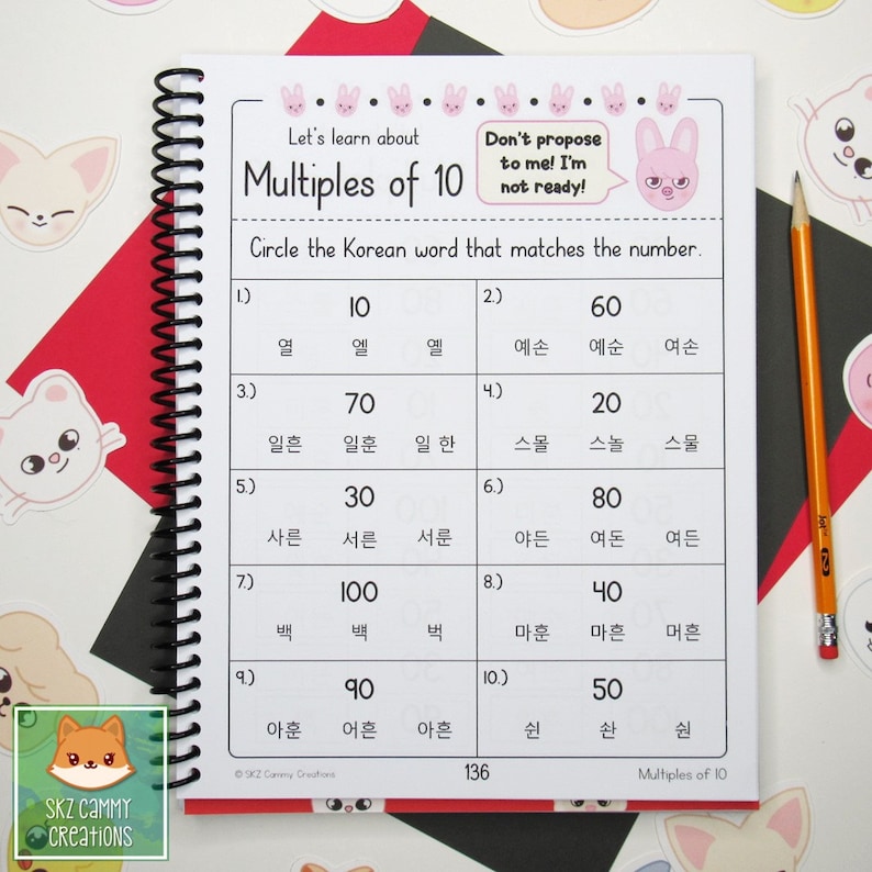 Pu&ograve; includere: Una pagina di quaderno a spirale con esercizi di apprendimento della lingua coreana. La pagina presenta il titolo "Multiples of 10" e include domande a scelta multipla. Una matita &egrave; appoggiata sulla pagina.