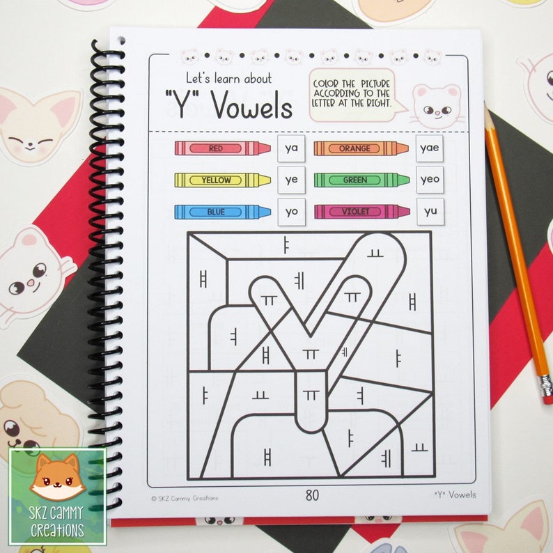 Pu&ograve; includere: Una pagina di quaderno a spirale con il testo "Let's learn about 'Y' Vowels". La pagina presenta un'attivit&agrave; di colorazione per lettera con pastelli e una legenda dei colori. Una matita &egrave; appoggiata sul lato destro della pagina. Il quaderno &egrave; su una superficie a motivi.