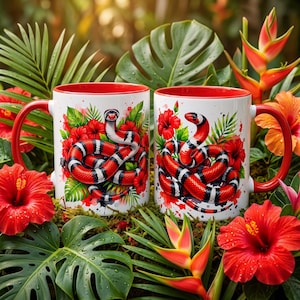 Peut inclure: Deux tasses en céramique blanche avec intérieur et anse rouges, ornées d'un motif coloré de serpent corail enroulé parmi des fleurs d'hibiscus rouges et un feuillage tropical vert, sur un fond de plantes de jungle luxuriantes et humides.
