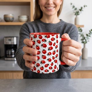 Może przedstawiać: Biały ceramiczny kubek z powtarzającym się wzorem czerwono-czarnych biedronek na zewnętrznej powierzchni. Kubek posiada wnętrze w kolorze jaskrawej czerwieni oraz pasujący czerwony uchwyt, co tworzy wyrazisty kontrast z białym tłem naczynia.