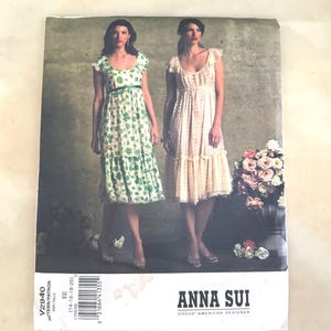May include: A Vogue American Designer sewing pattern envelope for Anna Sui dress V2940, size EE (14-16-18-20). The cover displays two variations of a knee-length dress with a scoop neckline, cap sleeves, and a tiered skirt, one in green floral.
