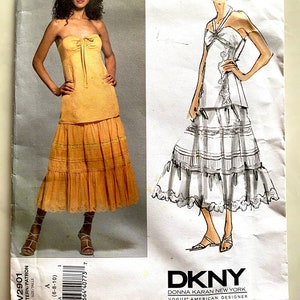 May include: A vintage sewing pattern with two dress designs. One is a strapless, tiered skirt dress in a golden colour. The other is a halter-top dress with a tiered skirt. The pattern is labeled "DKNY DONNA KARAN NEW YORK VOGUE AMERICAN DESIGNER".