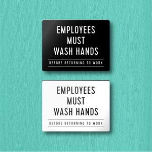 May include: Two signs, one black and one white, with the text "EMPLOYEES MUST WASH HANDS BEFORE RETURNING TO WORK".