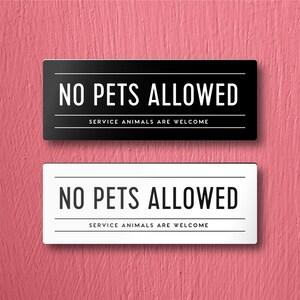May include: Two signs, one black and one white, with the text "NO PETS ALLOWED" and "SERVICE ANIMALS ARE WELCOME" in black lettering.