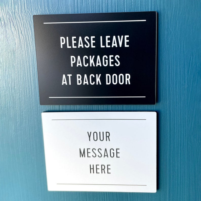 May include: Two signs on a blue wall. The top sign is black with white text that reads "Please Leave Packages At Back Door". The bottom sign is white with black text that reads "Your Message Here".