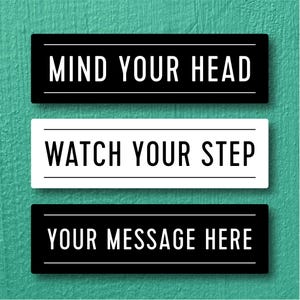 May include: Three rectangular signs with white text on a black or white background. The top sign reads "MIND YOUR HEAD", the middle sign says "WATCH YOUR STEP", and the bottom sign says "YOUR MESSAGE HERE". The signs are on a teal textured background.