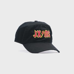 Puede incluir: Gorra de béisbol negra con visera curva. La gorra presenta el texto "JXMS" en rojo y amarillo, con acentos de rayos. El sombrero está hecho de un material suave y tiene una corona redondeada.