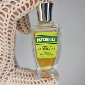 May include: A small glass bottle of Patchouly perfume de toilette by Rene Pascal Paris London. The bottle is clear and contains a yellow liquid. The label is green and yellow with the words "Patchouly" and "Parfum de Toilette" in black.