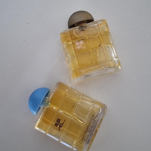 Może przedstawiać: Dwa małe szklane flakoniki perfum z wzorem kratki. Buteleczka po lewej stronie ma niebieską zakrętkę i tekst "Courages in blue 5ml - 85% vol. Eau de Toilette" na etykiecie. Buteleczka po prawej stronie ma brązową zakrętkę i tekst "Courreges" na etykiecie.