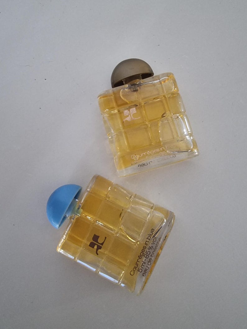 Może przedstawiać: Dwa małe szklane flakoniki perfum z wzorem kratki. Buteleczka po lewej stronie ma niebieską zakrętkę i tekst "Courages in blue 5ml - 85% vol. Eau de Toilette" na etykiecie. Buteleczka po prawej stronie ma brązową zakrętkę i tekst "Courreges" na etykiecie.