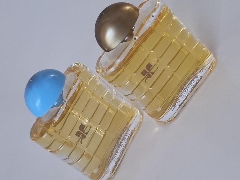 Może przedstawiać: Dwa małe szklane flakoniki perfum z złotymi i niebieskimi nakrętkami. Flakoniki są przezroczyste i mają kratkę na przodzie. Tekst na flakonikach brzmi "Paris 5 ml 80% vol."
