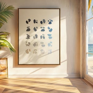 May include: A framed abstract art print featuring a series of blue and gray organic shapes on a cream background. The artwork is displayed on a white wall, with a wooden floor and a view of the ocean through a window.