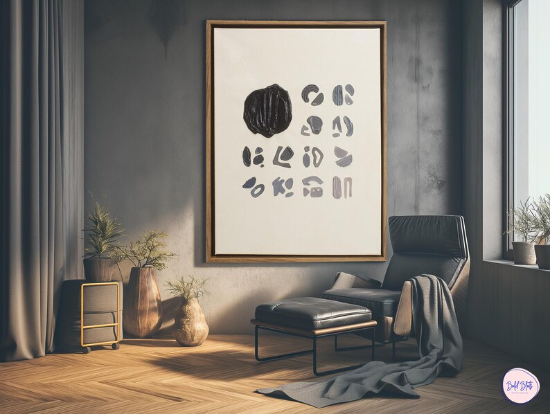 May include: A black and white abstract art print with a large black shape in the center and smaller shapes surrounding it. The print is framed in a light wood frame and is hanging on a gray wall. A black leather armchair with a footrest is in the foreground.