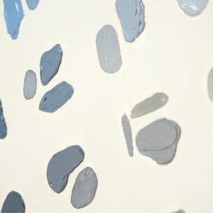 May include: Close-up of a canvas with a cream-colored background. The canvas is decorated with irregular, abstract shapes in shades of blue and gray. The shapes are painted with visible brushstrokes, creating a textured effect.